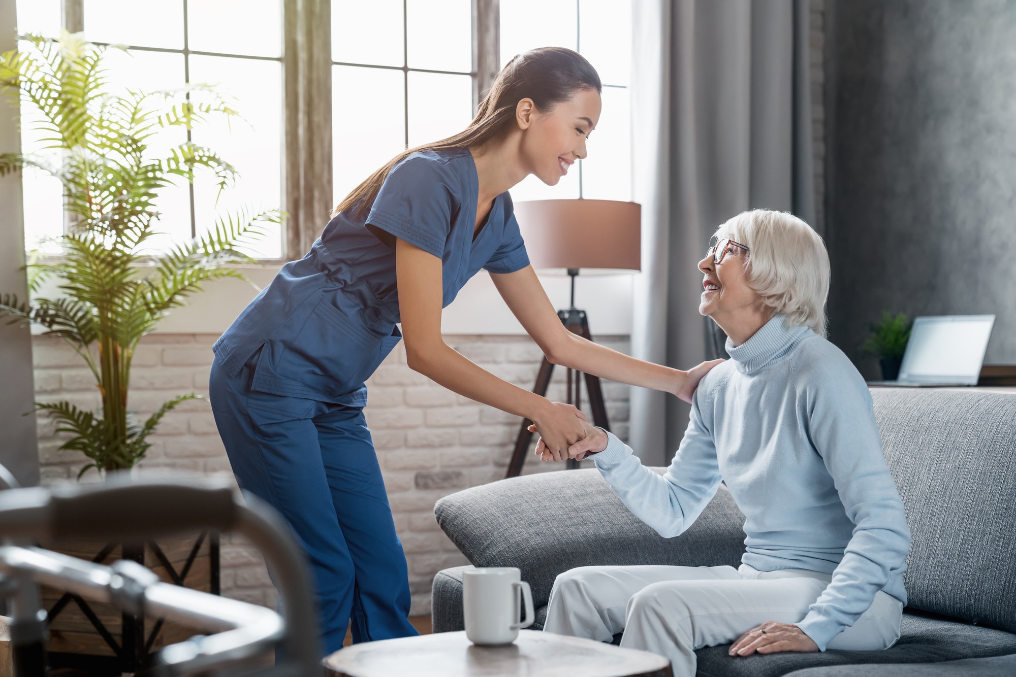 Happy female professional caregiver taking care of elderly woman at home